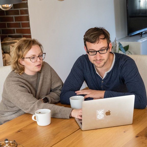 Ehepaar sitzt am Tisch und arbeitet gemeinsam am PC